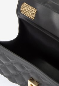 Borsa a tracolla nera trapuntata con una texture liscia, dotata di una placca in hardware color oro e un interno che sembra spazioso e foderato in tessuto.