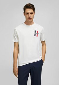 Wit T-shirt met korte mouwen met een grafisch ontwerp van rood, marineblauw en witte verticale strepen en de tekst "HECHTER" op de linkerborst.