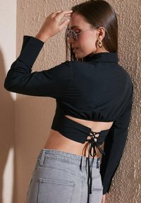 Black long-sleeve cropped top with a stretchy back, featuring a lace-up detail. Paired with light gray high-waisted denim jeans.