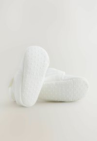 Vita babyskor med mjukt tygöverdrag och texturerade gummisålar. Kännetecknas av "NEXT baby"-logotypen och prickmönster på sålarna.