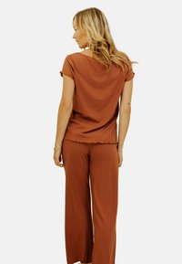 Haut côtelé couleur rouille avec des manches courtes et un pantalon large assorti. Texture douce avec une coupe décontractée et des détails d'ourlet.