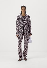 Two-piece suit featuring a black and pink floral pattern. The jacket has a lapel collar, and the pants are tailored. Accessories include a white bag.