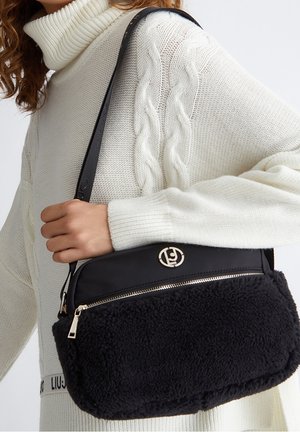 Sac à main noir avec un corps en tissu pelucheux et texturé, une quincaillerie dorée et une fermeture éclair supérieure. Comprend une sangle en cuir lisse et un accent logo.