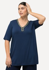 Námořnická modrá krátká halenka s výstřihem do V, zdobená dekorativními korálky kolem výstřihu a volným střihem. Měkká textilie.