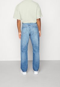Jeans in denim blu chiaro con vestibilità dritta, caratterizzati da tasche posteriori e vita alta. Indossati con una t-shirt oversize verde chiaro.