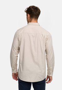 Beige langærmet skjorte med knappespænde krave, enkel knapmanchetter og en buet kant, lavet af et let, tekstureret stof.