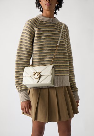 Bolso acolchado blanco con cadena dorada, que cuenta con un cierre decorativo. Combinado con un suéter a rayas y una falda beige con pliegues.
