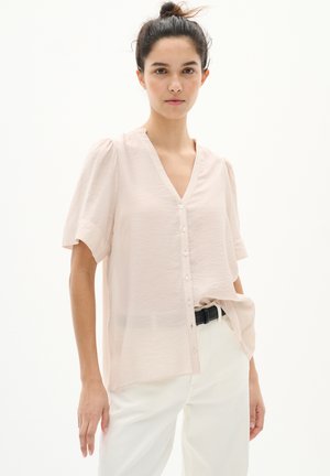 Blusa rosa chiaro con scollo a V, maniche a puff corte e chiusura con bottoni. Realizzata in un materiale morbido e strutturato, abbinata a pantaloni bianchi e una cintura nera.