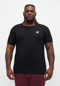 Tricou scurt, negru, din bumbac, cu guler rotund. Prezintă un mic logo alb pe pieptul stâng. Textură fină.