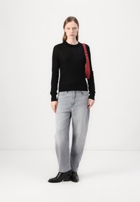 Svart strikkegenser, lys grå baggy jeans og svarte ankelboots. En rød stropp bæres over kroppen, som gir en kontrasterende aksent.