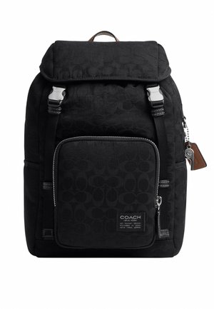 Mochila negra de Coach con bolsillo delantero con cremallera, dos correas con hebilla, asa de cuero y etiquetas de la marca colgando a un lado.