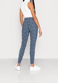 Blue patterned leggings with a slim fit, featuring an elastic waistband and a textured design, paired with white athletic shoes.
