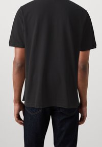 T-shirt noir à manches courtes avec un col ras du cou, en tissu lisse. Doté d'un ourlet droit et d'échancrures latérales, associé à un jean en denim foncé.