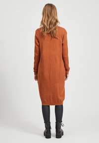 Lång, figurnära stickad klänning i bränd orange, med ribbade ärmslut och fåll. Matchad med svarta leggings och kraftiga ankelskor.