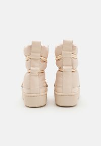 Beige polstret høyt topp sneakers med elastiske lisser og synlige sømmer, med en teksturert gummisåle og forsterkede hælknotter.