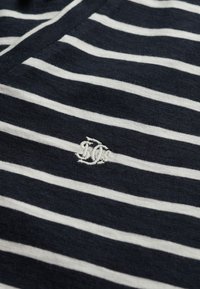 Granatowo-biały pasiasty materiał o miękkiej fakturze; na środku znajduje się wyhaftowane białe logo. Krój z dekoltem w serek.