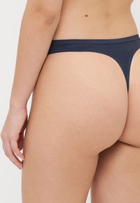 Granatowe stringi Calvin Klein wykonane z gładkiego, miękkiego materiału z cienkim pasem i minimalnym kryciem, prezentujące bezszwowy design.