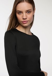 Czarna bluzka z długim rękawem, wykonana z gładkiego, elastycznego materiału. Posiada okrągły dekolt i dopasowany fason, z długimi rękawami i minimalnymi detalami.