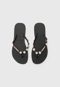 Μαύρες ελαστικές παντόφλες με υφή στο πέλμα, διακοσμημένες με λουλουδάτο χάντρα και λεπτομέρεια λογότυπου στη λουρίδα. Ελαφρύ και casual σχέδιο.