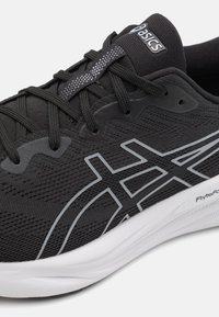Scarpa sportiva nera con tomaia in tessuto testurizzato, dettagli riflettenti e suola bianca. Presenta un design del logo grigio prominente sul lato.
