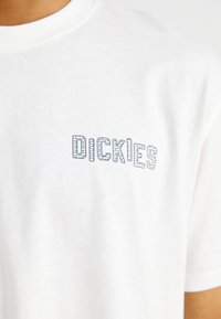 White cotton t-shirt featuring a printed logo that reads "DICKIES" in gray with a block-style design on the left chest area.