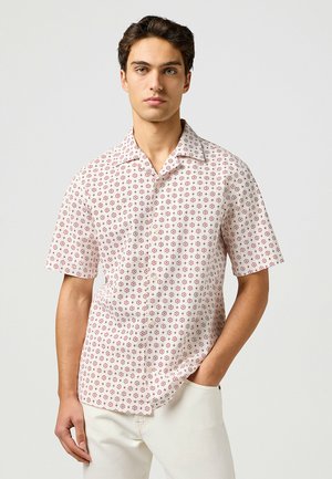 Chemise à manches courtes en tissu léger, ornée d'un motif floral rouge sur fond clair, avec un col classique et une coupe décontractée.