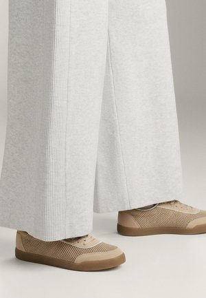 Světle šedé široké kalhoty vyrobené z měkké látky, spárované s béžovými síťovými teniskami s texturovaným svrškem a gumovou podrážkou.