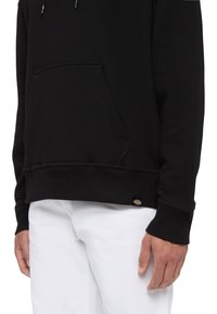 Sudadera negra de mezcla de algodón con un bolsillo frontal, puños y dobladillo acanalados. Presenta una pequeña etiqueta con el logotipo en la parte inferior izquierda.