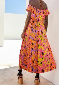 Robe maxi décolletée avec des motifs floraux vibrants en rose, orange et jaune. Tissu texturé, taille élastique et manches à volants.