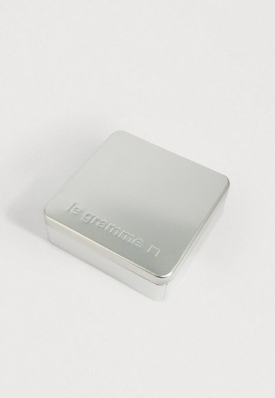 Scatola metallica rettangolare argento con bordi curvi e "le gramme" imprintato sul coperchio, posizionata su una superficie bianca semplice.