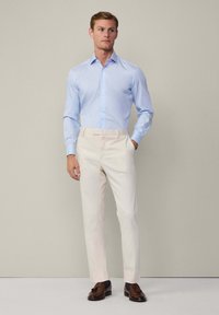 Lichtblauwe button-up shirt, beige op maat gemaakte broek en bruine loafers. Soepele stoffen, slim fit ontwerp en strakke lijnen. Neutrale achtergrond.