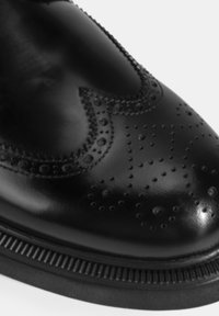 Zwarte leren schoen met brogue-details, voorzien van perforaties, een gladde afwerking en een getextureerde zwarte zool.