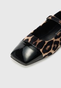 Chaussure Mary Jane en suède à imprimé léopard, avec un bout carré en vernis noir et une fine sangle. Présente une texture lisse et des bords arrondis.