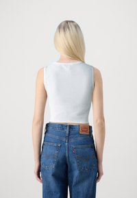 Bílý žebrovaný bezrukávový crop top s kulatým výstřihem, zkombinovaný s vysokým modrým denimovým džíny, které mají koženou nášivku na zadní straně.