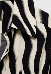 Cămașă cu model zebra în alb și negru, cu mâneci scurte, realizată dintr-un material texturat cu dungi ondulate și guler ascuțit.