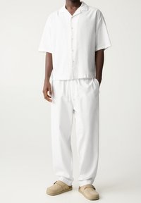 Witte linnen korte mouwen blouse met knoopsluiting en ontspannen pasvorm witte broek. Lichtgekleurde instapschoenen maken de outfit compleet.