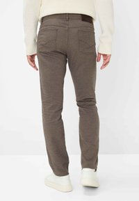 Braun strukturierte Slim-Fit-Jeans mit Gesäßtaschen. Kombiniert mit einem kontrastierenden Bund und weißen Sneakers. Lässiges, figurbetontes Design.