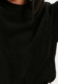 Maglione in pile nero con scollo tondo, maniche lunghe e una morbida e testurizzata stoffa. Il design ha una vestibilità comoda e dettagli minimi.