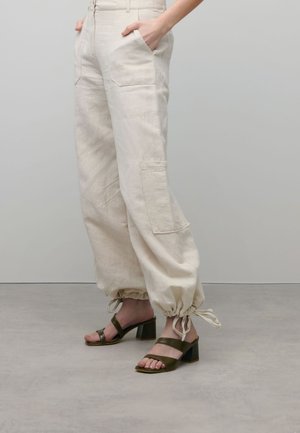 Beige linnen cargo broek met elastische enkelmanchetten, inclusief voorkruim pockets. Gecombineerd met olijfgroene blokhak sandalen met kruislings banden.