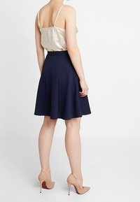 Marinblå A-linjeformad kjol med en texturerad yta, ihop med en satinbeige topp och nudefärgade högklackade skor. Synliga sömmar och en figurnära midja.