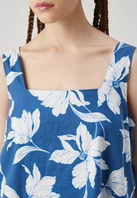 Blue floral top featuring a square neckline, made from a textured fabric with white flower patterns, showcasing light and dark contrasts.