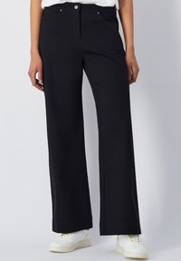 Zwarte wijde broek van een katoenmix, met steekzakken aan de voorkant en een knoopsluiting. Draagt met witte sneakers voor contrast.