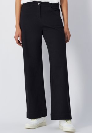 Zwarte wijde broek van een katoenmix, met steekzakken aan de voorkant en een knoopsluiting. Draagt met witte sneakers voor contrast.