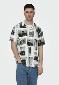 Camicetta a maniche corte con stampe fotografiche in bianco e nero, dal design rilassato, realizzata in tessuto leggero, abbinata a jeans in denim blu.
