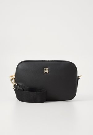 Zwarte rechthoekige crossbodytas met gouden hardware en logo, en een brede verstelbare stoffen riem opgerold aan de voorkant op een effen achtergrond.