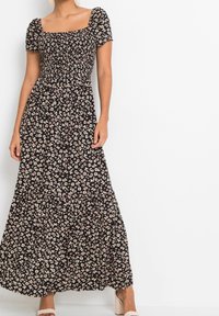 Maxi šaty z černé látky s květinovým vzorem v bílé a růžové barvě. Mají upnutý korzet, nabírané rukávy a vrstvený design sukně.