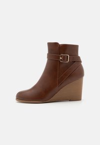 Brune faux læder ankelstøvle med kilehæl, sidespænde detalje og glat overflade. Rund tå og ribbet såldesign.
