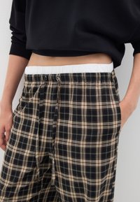 Pantalons de pyjama à carreaux noirs et beiges avec une taille élastique et un cordon de serrage, dotés d'une coupe ample et de poches latérales.