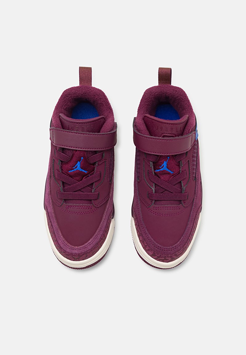 Zapatillas color burdeos con una parte superior texturizada, cuello acolchado y detalles en azul. Las características incluyen una correa, cordones y una suela blanca en contraste.