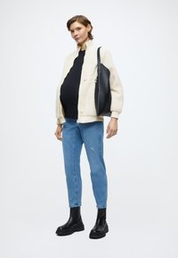 Giacca in pile color crema con accenti neri, top nero aderente, jeans azzurri e stivali neri con tacco largo, porta una borsa nera.